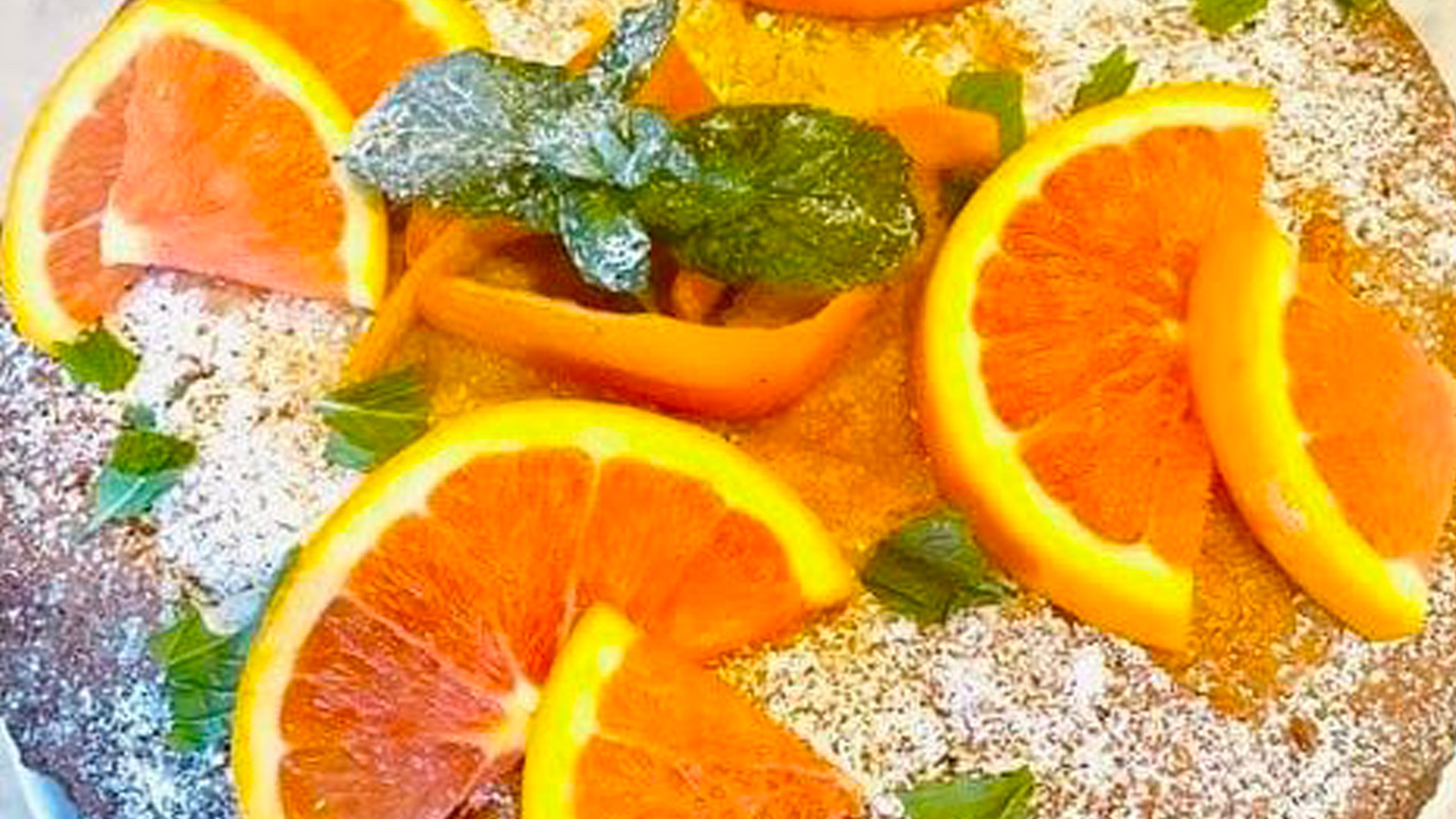 A top view of an orange olive oil cake garnished with orange slices and mint leaves.