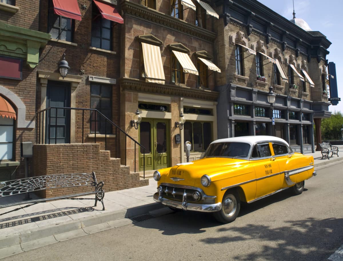 Vintage yellow cab parked outside brick buildings.
