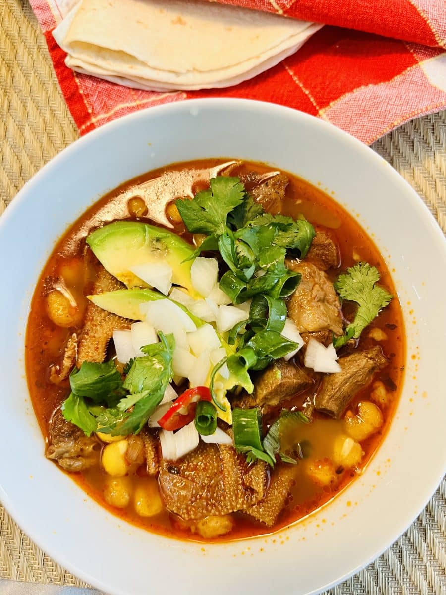 A bowl of Menudo Rojo garnished with cilantro, avocado, and onions.