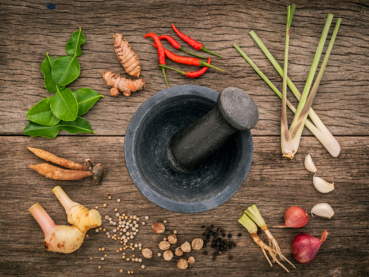Assortment of Thai ingredients and a stone mortar and pestle on a rustic wooden background.