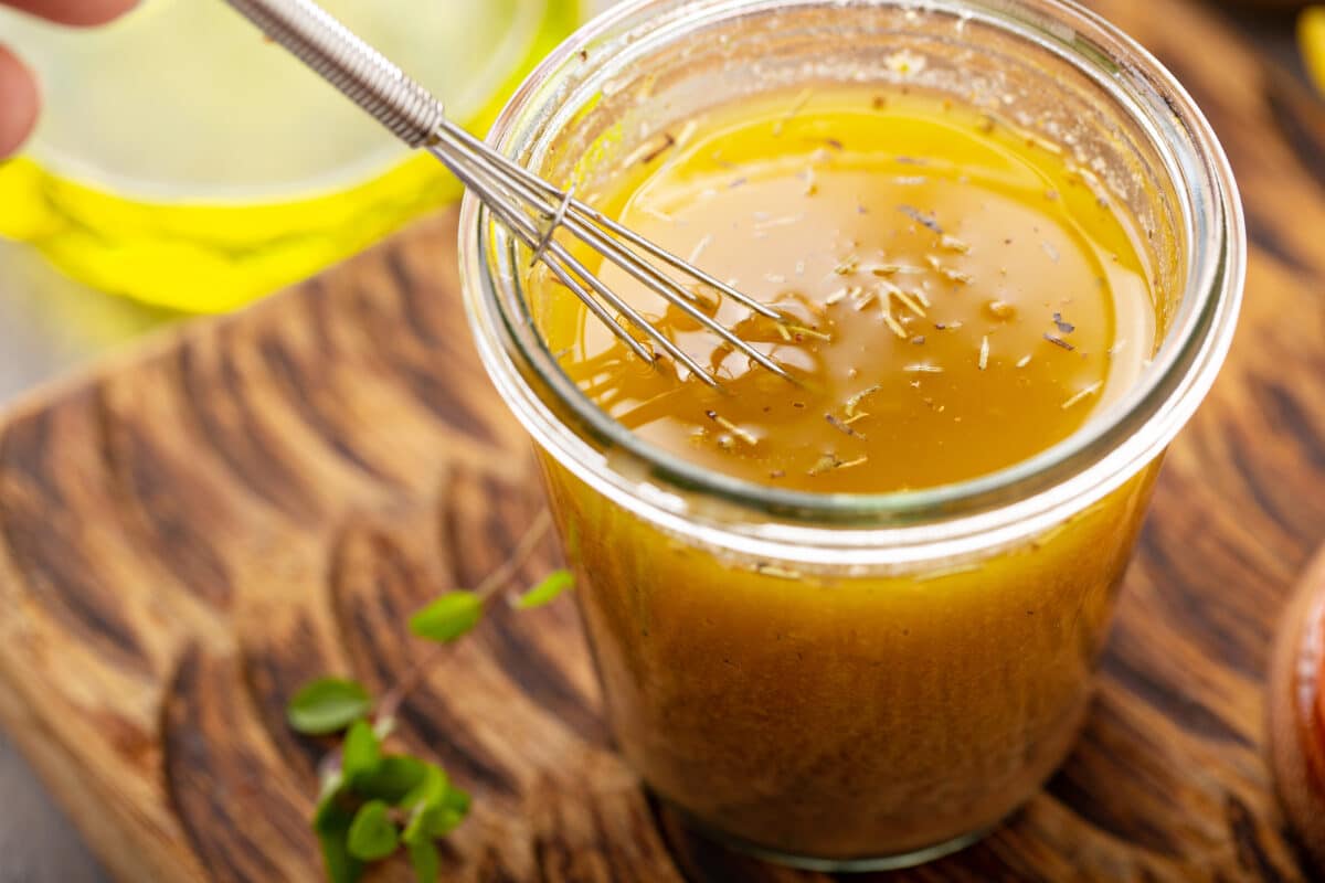Salad dressing with olive oil and herbs in a jar with a small whisk