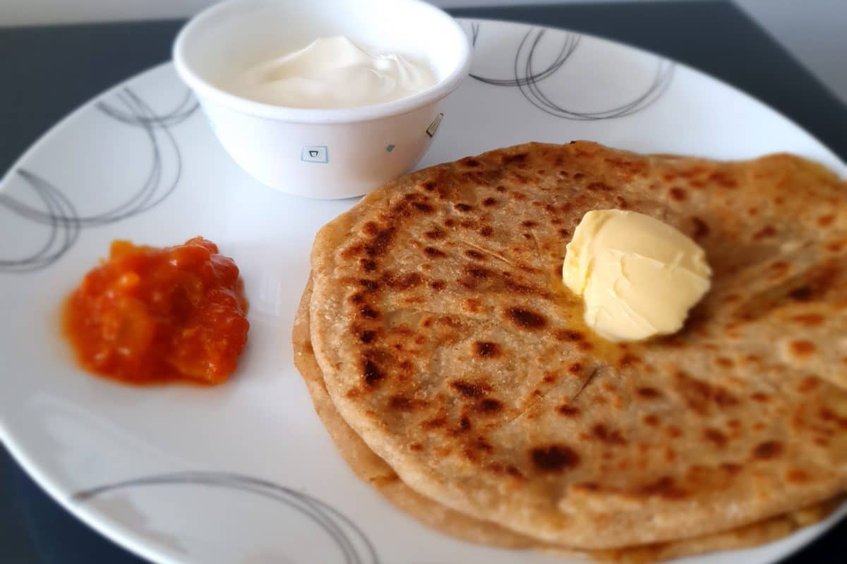Close-up view of Aloo Paratha with white and orange dips.