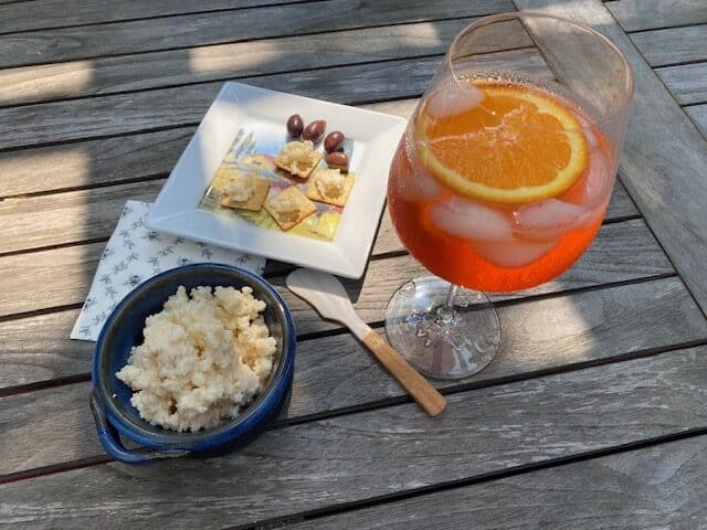 A view of an Aperol Spritz drink and a cicchetto on a wooden table