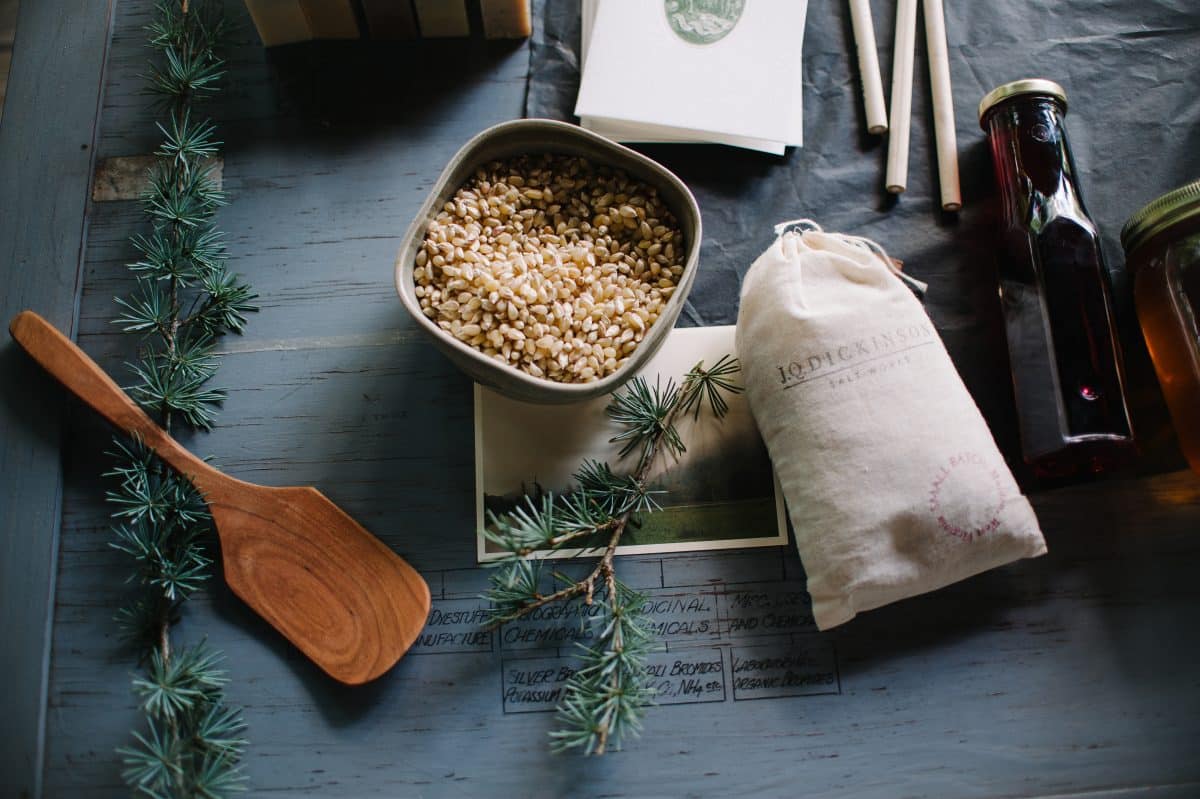 Appalachian mercantile products on a table with a bowl of grains, bottles, and wooden spoon.