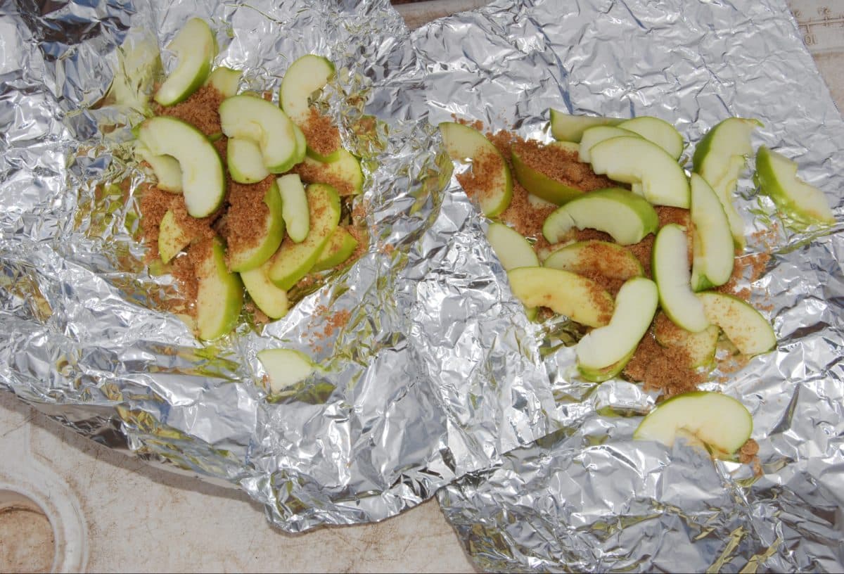 Slices of apples sprinkled with spices on aluminum foil, ready for baking.