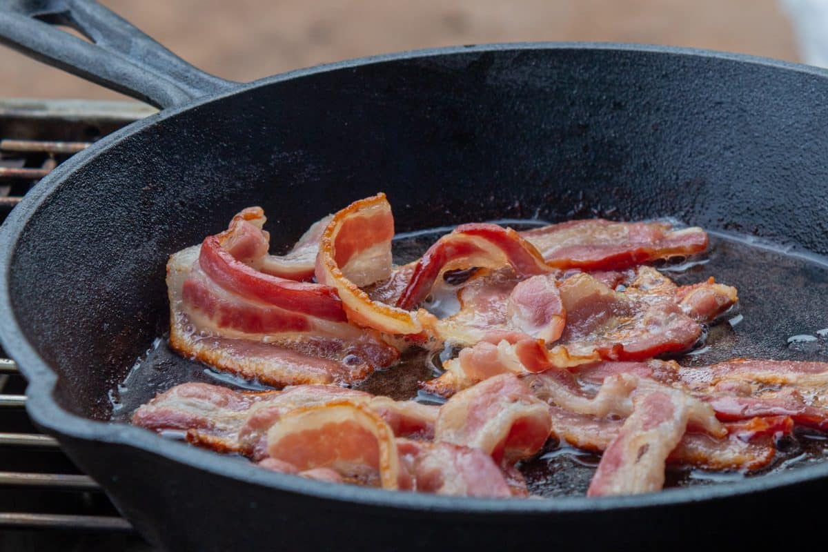 Strips of bacon frying in a cast-iron skillet.