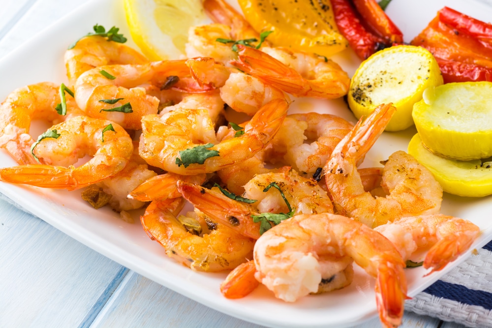 Delicious garlic butter roasted shrimps paired with colorful summer vegetables on a plate.