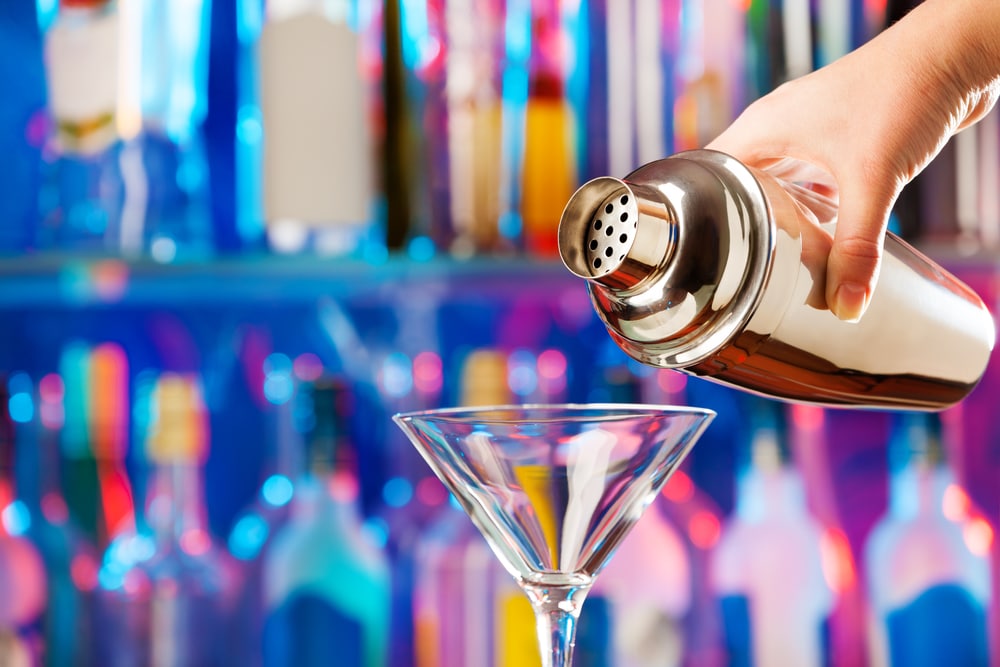 Barman's hand pouring a drink from a shaker into a cocktail glass.
