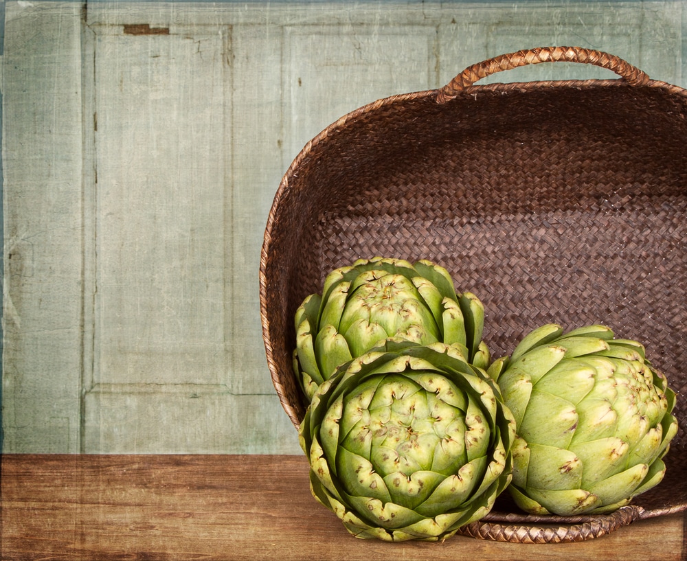 Close-up of fresh artichokes spilling out of a woven basket on a wooden surface.