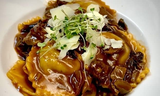 Ravioli with beef cheeks filling, garnished with greens.