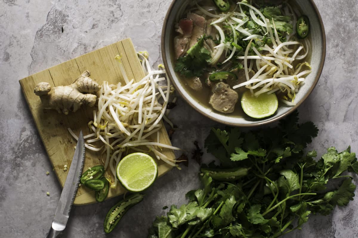 Bowl of beef pho with toppings like sprouts, cilantro, and lime.