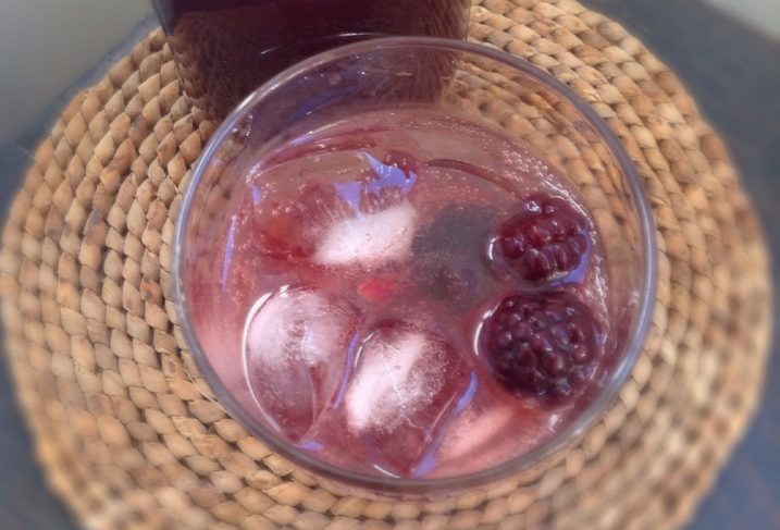 Top-down view of a drink with blackberries and ice on a woven coaster.