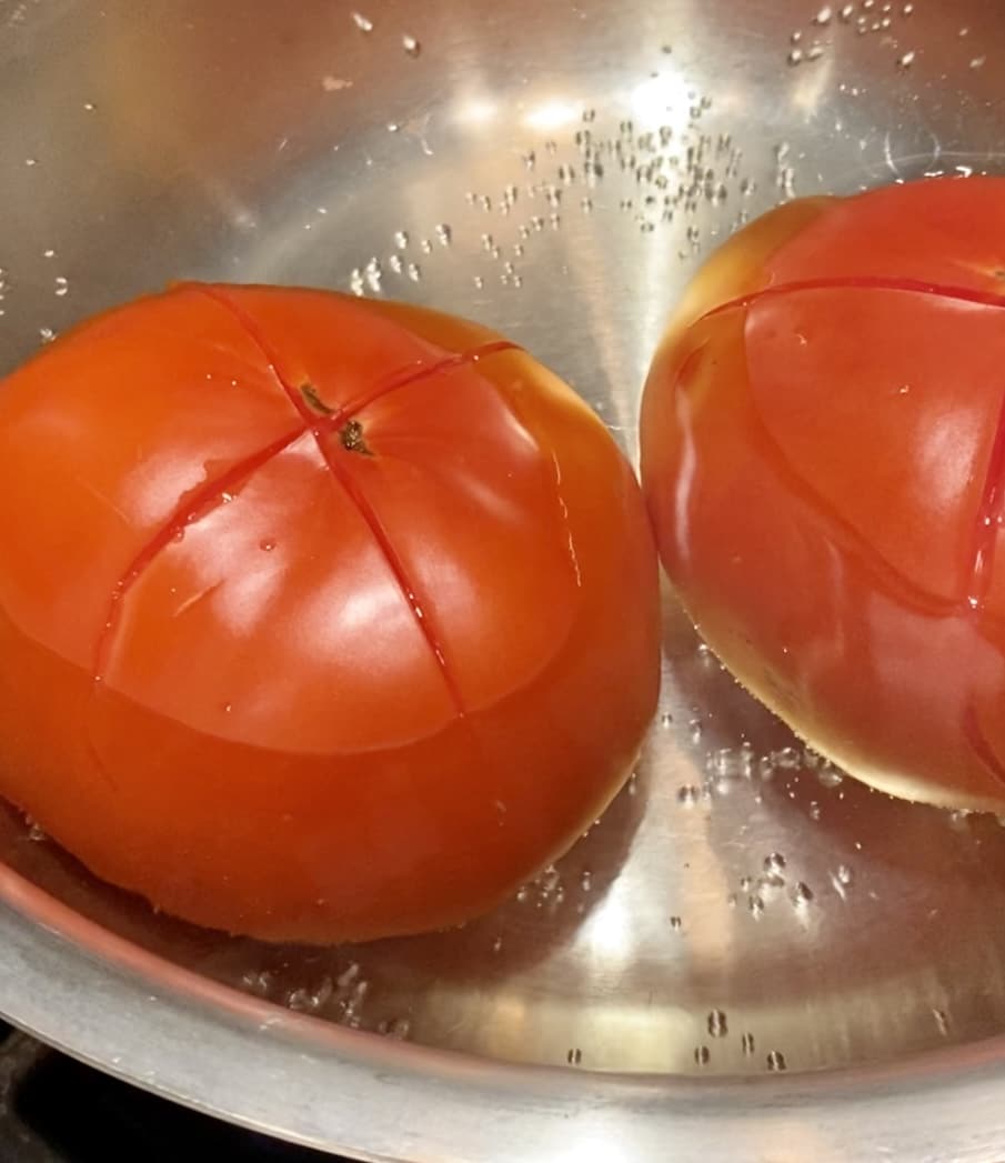 Two blanched tomatoes in a steel bowl.