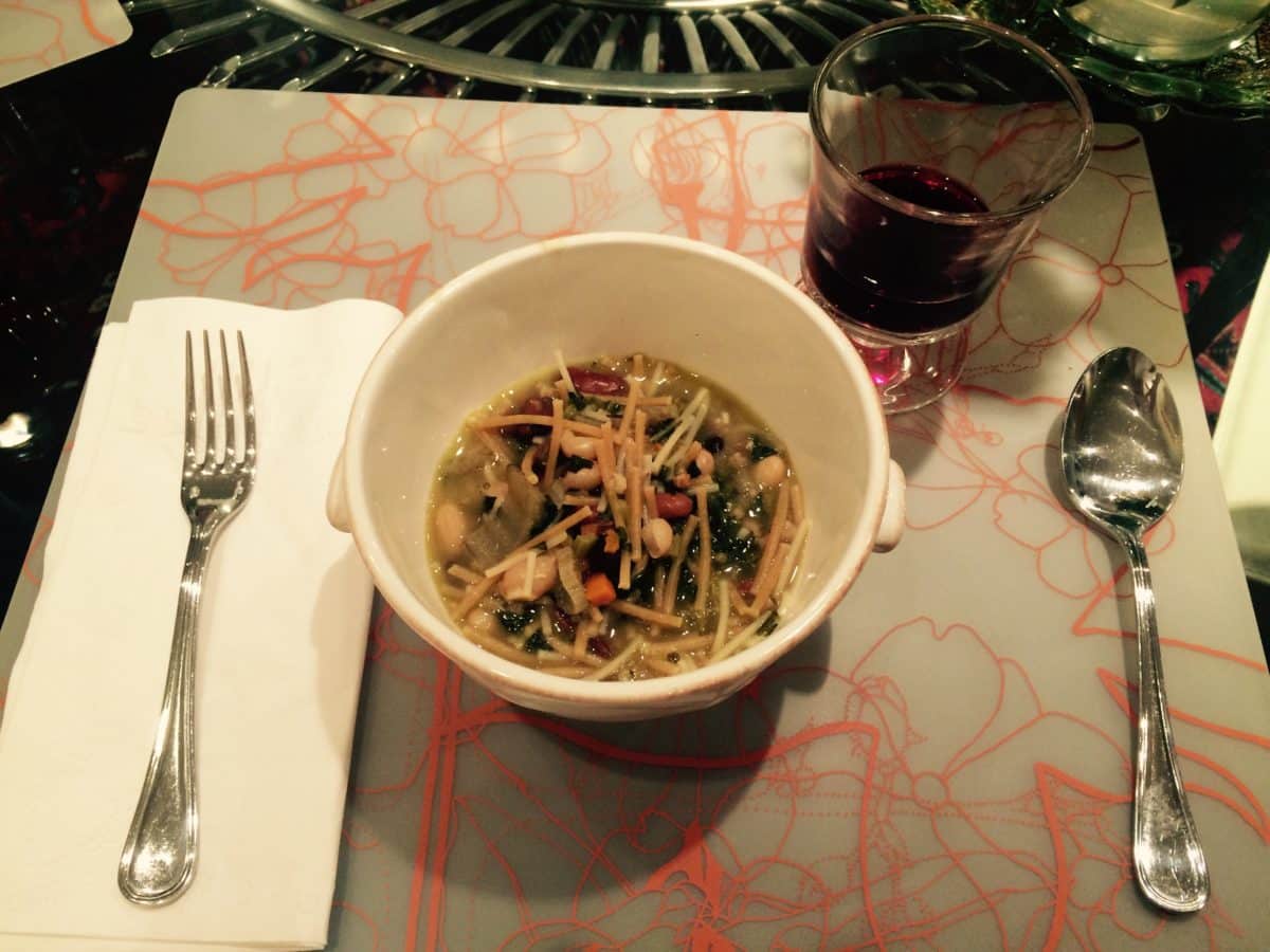 A bowl of Fagioli soup next to a glass of red wine