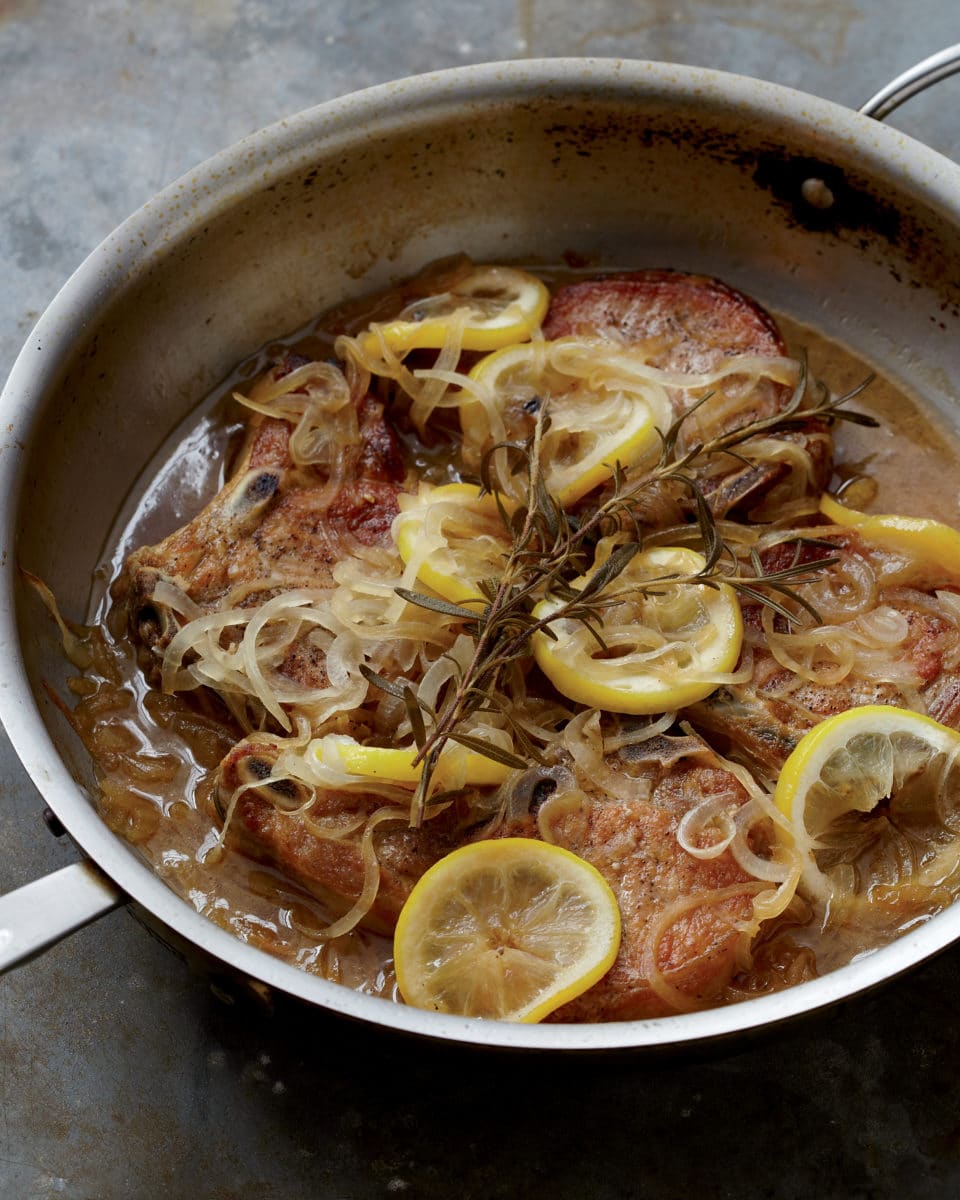 Braised pork chops in a pan with citrus garnish