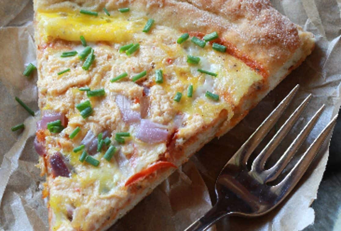 Close-up of a slice of breakfast pizza topped with cheese, eggs, onion, and chive.