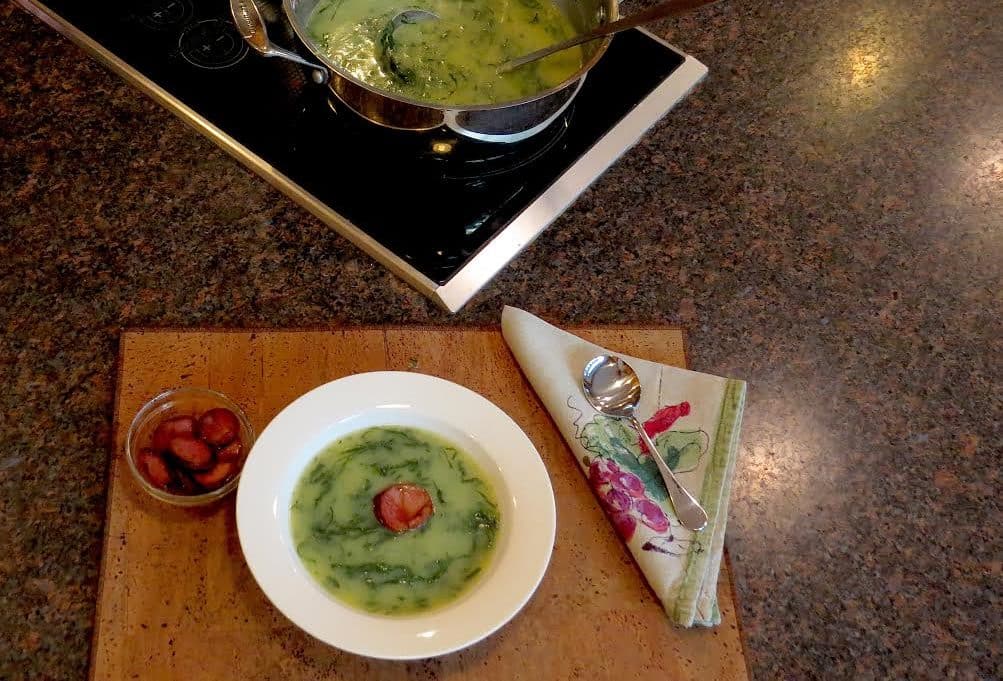 Caldo Verde soup served in a white dish with a tomato garnish