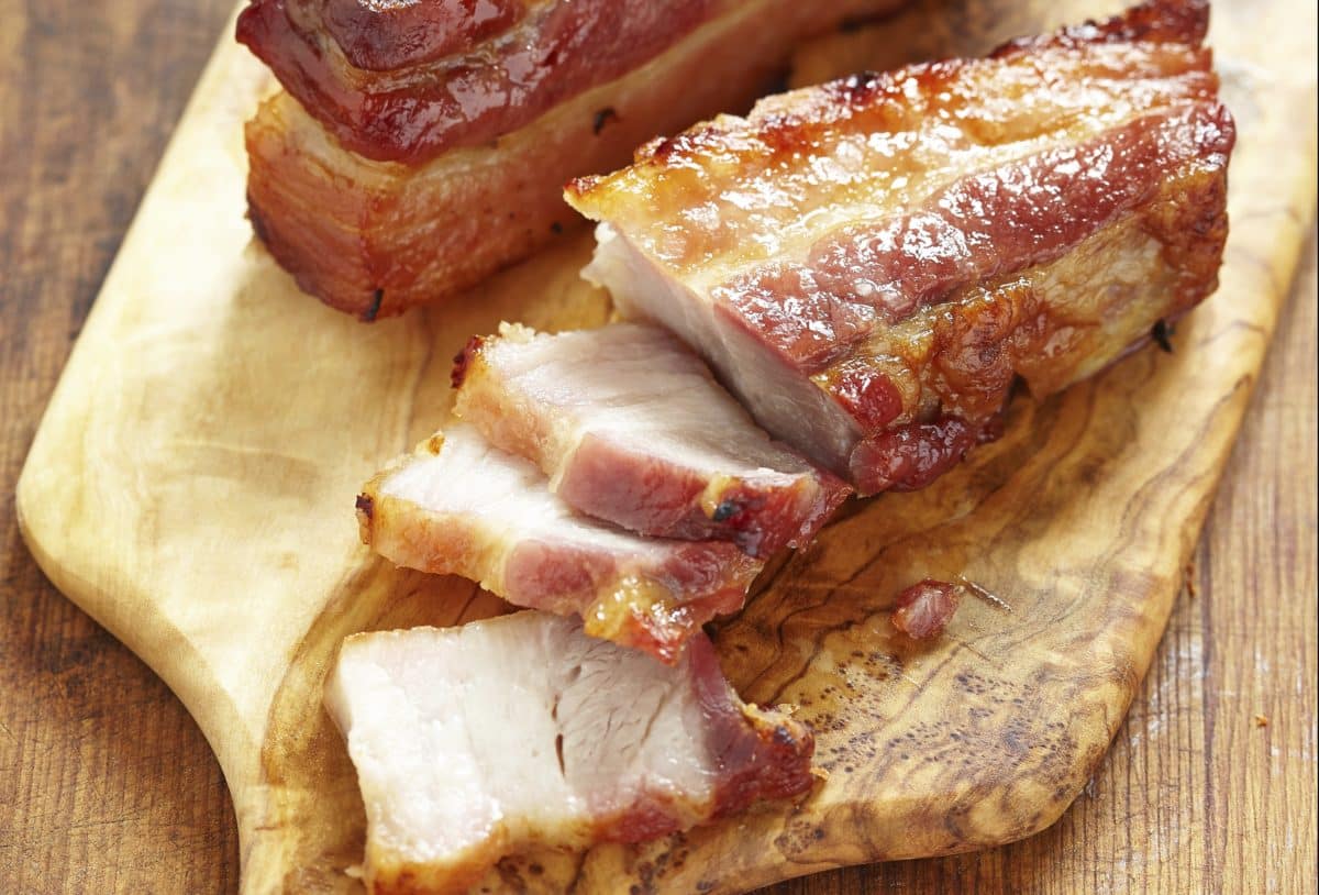 Sliced caramelized pork belly arranged on a rustic wooden cutting board.