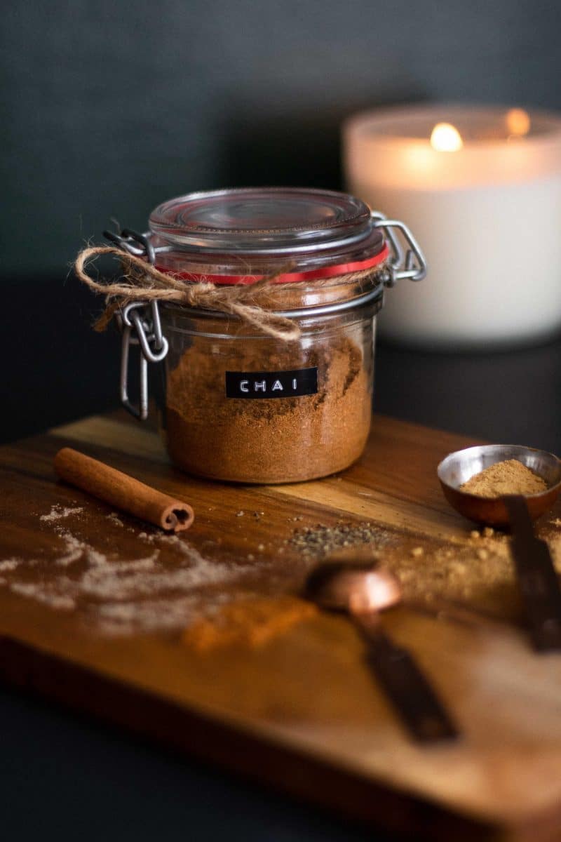 Chai masala powder in a glass jar with cinnamon stick on side.