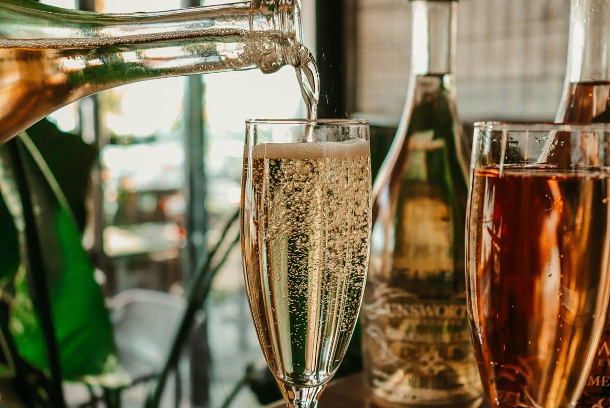 Close-up of champagne being poured into a glass next to a bottle of rose wine.