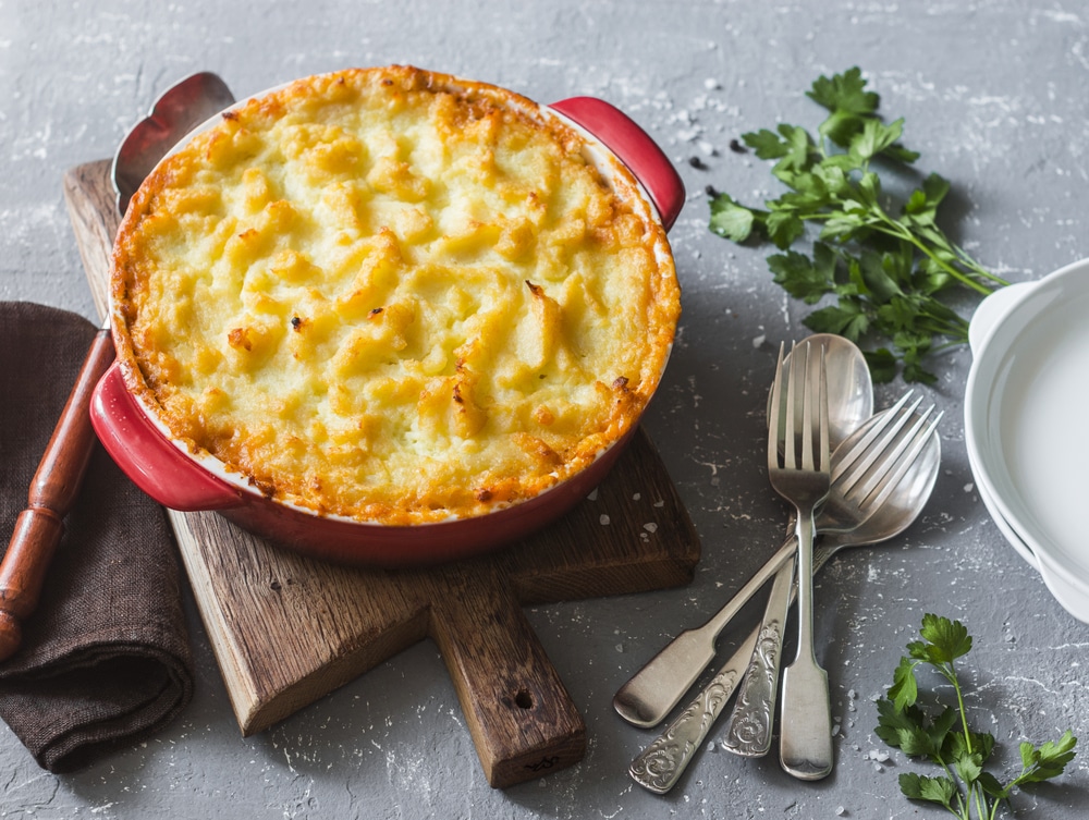 Potato Cheddar casserole in a red dish, served on a wooden board.