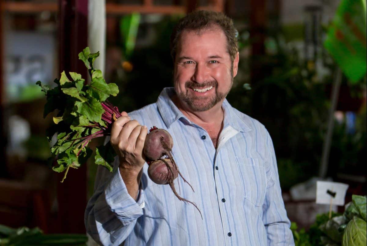 Chef Allen Susser smiling while holding a bunch of fresh beets