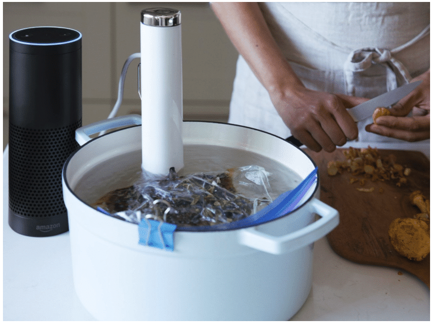 Chef using the ChefSteps Joule Sous Vide device to prepare food in a pot of water next to an Amazon Echo device.