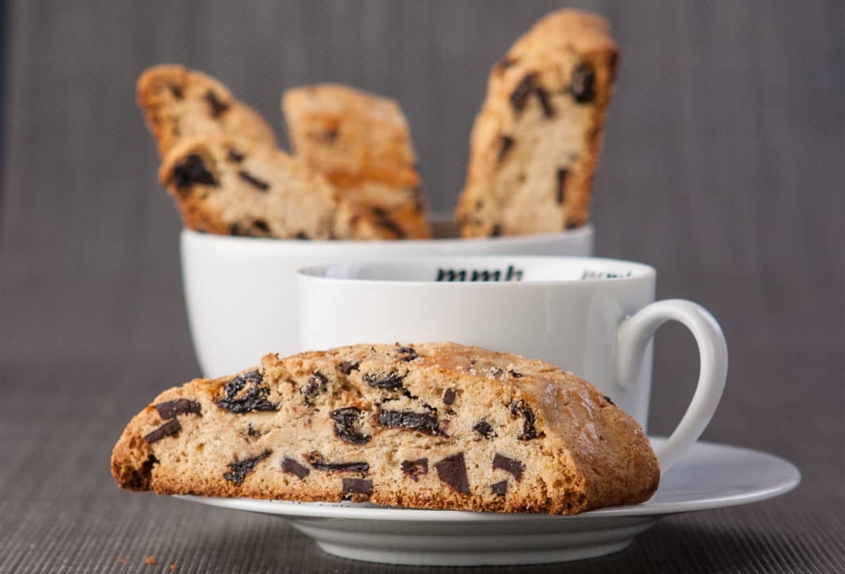 Cherry Chocolate Mandelbrot cookies beside a cup of white coffee cup.