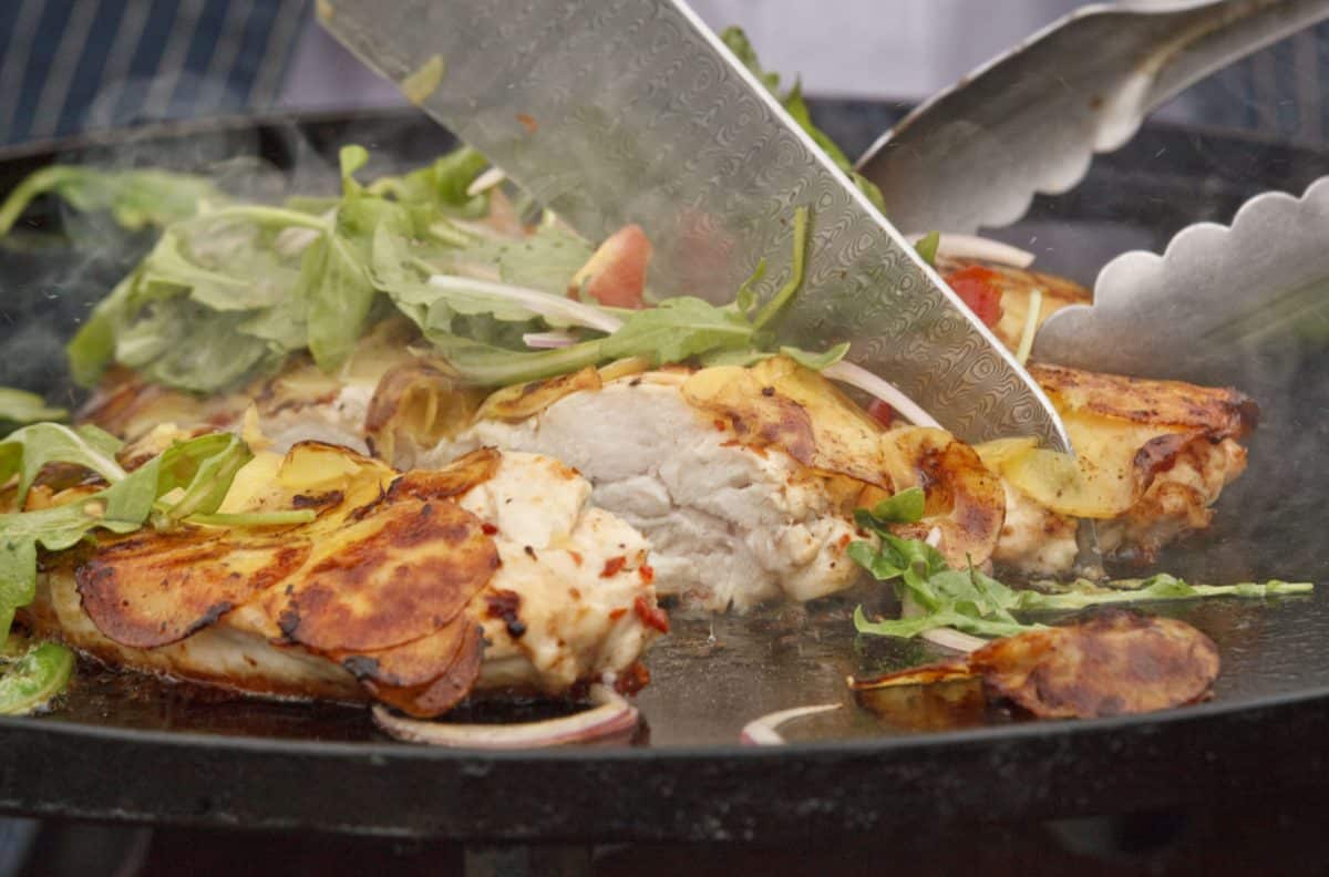 A chef preparing smashed chicken breast in a potato crust, topped with tomato and arugula salad.
