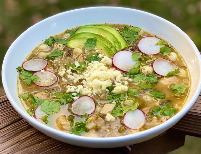 A bowl of Chicken Pozole Verde garnished with avocado, radishes, and cheese.