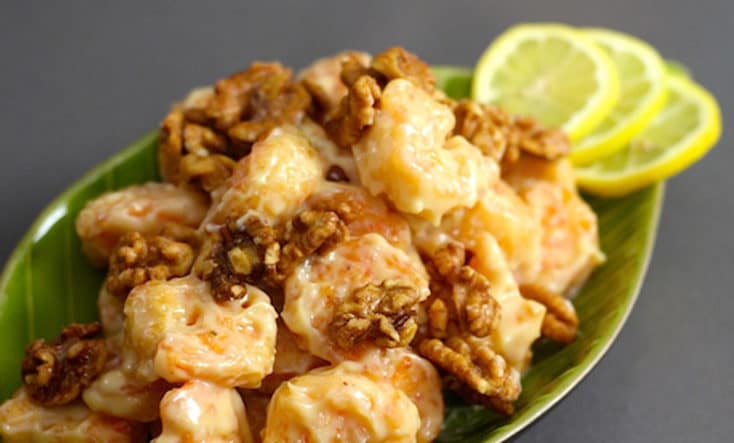 Delicious Chinese Walnut Shrimp served with a slice of lemon on a green leaf plate.