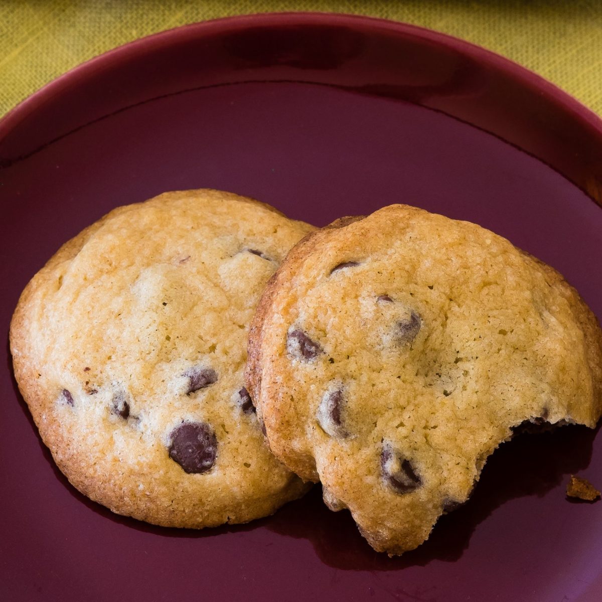 Two chocolate chip cookies on a burgundy plate.