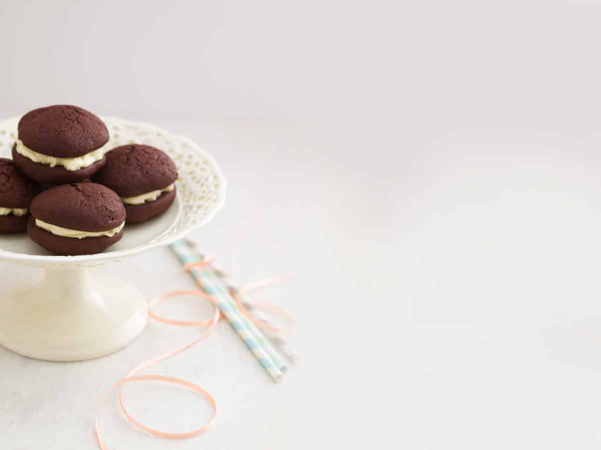 Chocolate whoopie pies with a creamy buttercream filling on a cake stand.