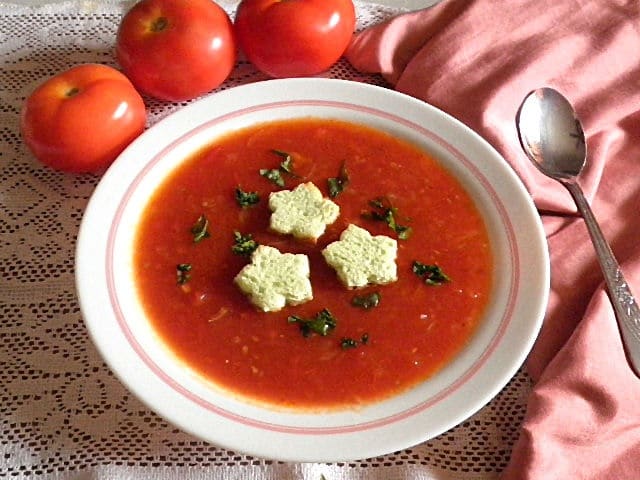 Bowl of tomato soup with croutons and fresh herbs on top.