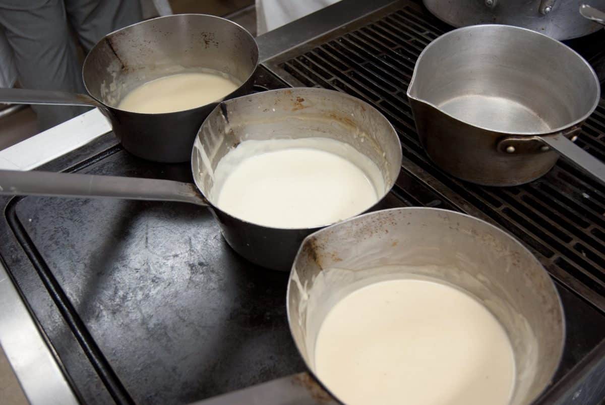 Three pots on a stovetop, each containing a different type of classic French sauce in preparation.