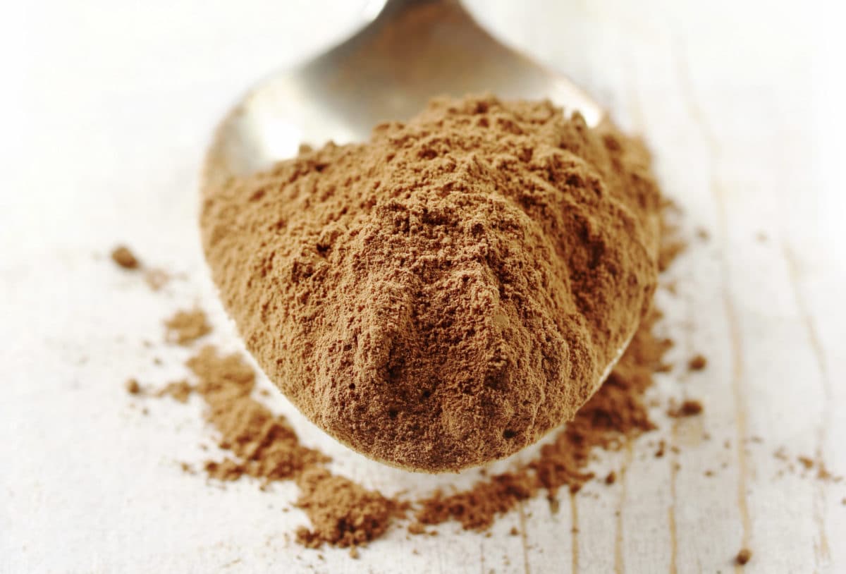 Finely ground cocoa powder resting on an antique silver spoon, placed on a weathered timber table.