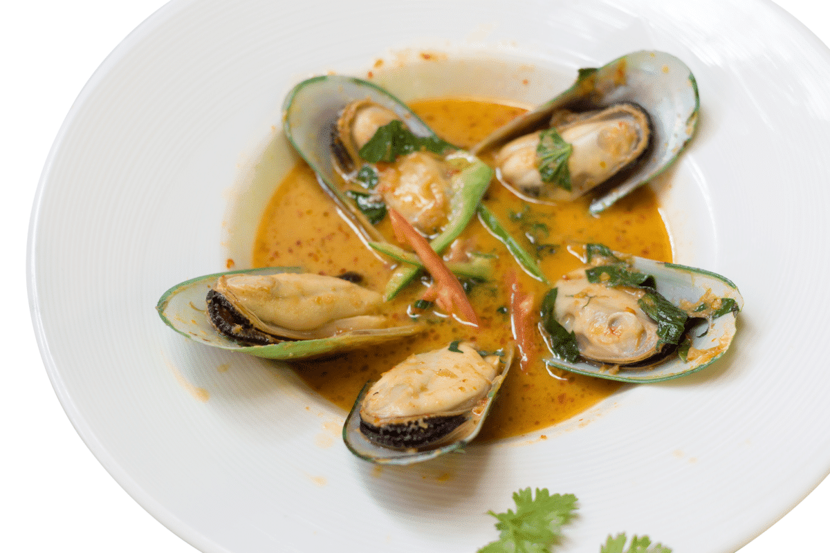 A dish of mussels in coconut curry sauce served on a white plate.
