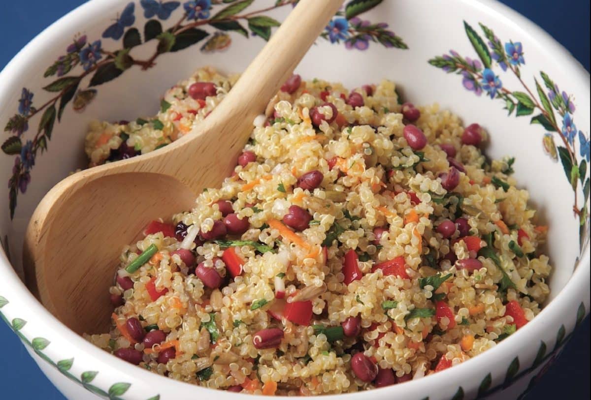 A floral bowl filled with colorful quinoa salad, garnished with beans and veggies, accompanied by a wooden spoon.