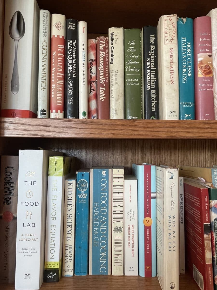 A wooden shelf displaying various cookbooks.