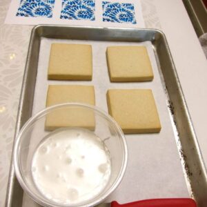 Plain rectangular cookies on a tray next to a bowl of white icing.
