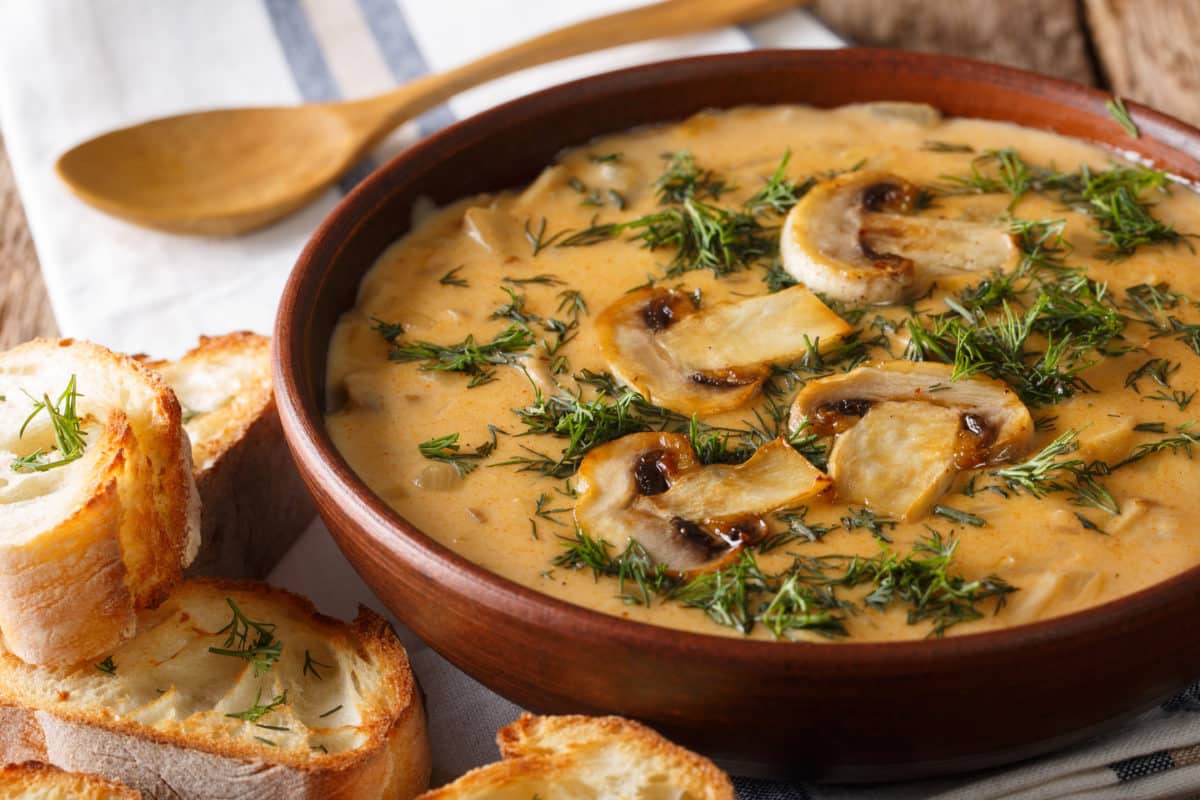 Bowl of creamy mushroom soup garnished with dill and accompanied by toasted bread.