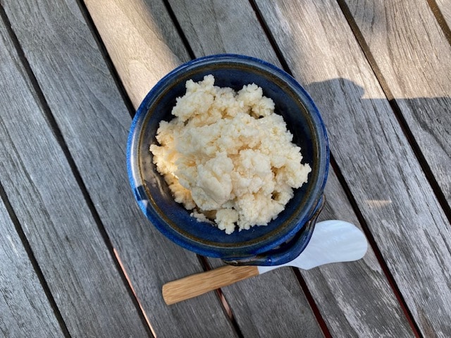 A blue bowl containing Crema di Parmigiano spread with a wooden spreader