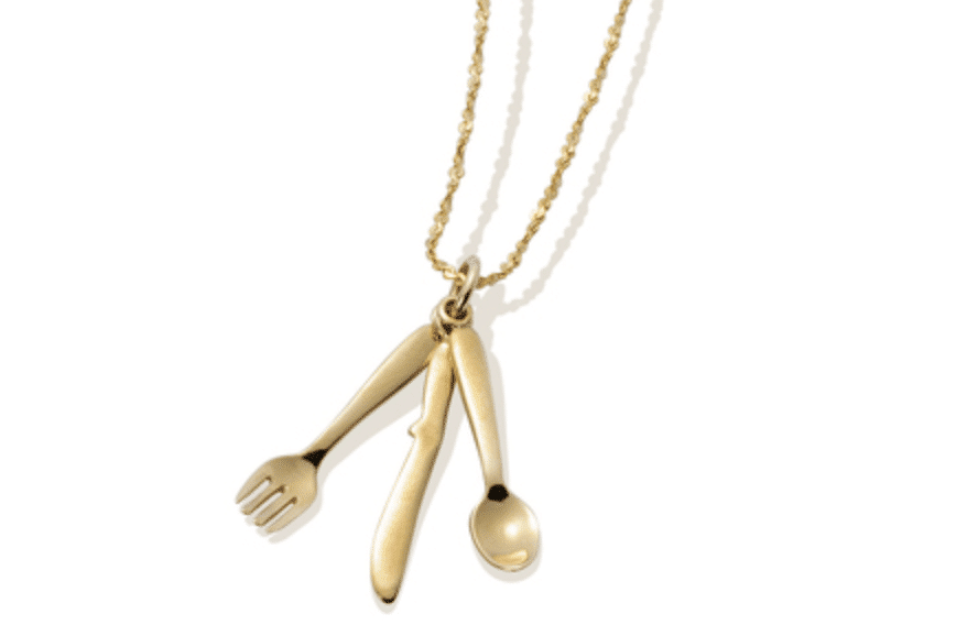 Gold cutlery pendant on a white beaded necklace.