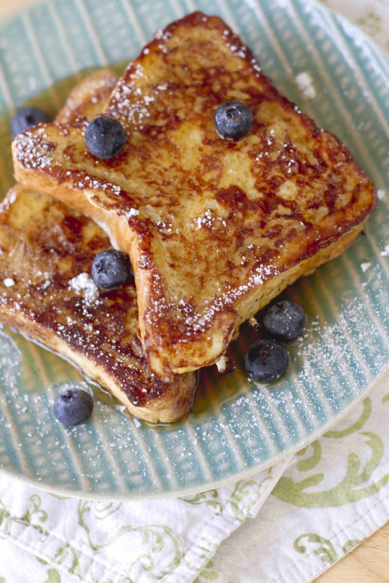 French toast topped with blueberries, powdered sugar, and maple syrup on a patterned plate.