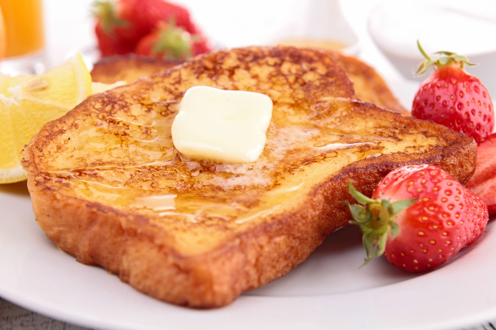 Golden brown French toast served with butter, honey, and strawberries on a white plate.