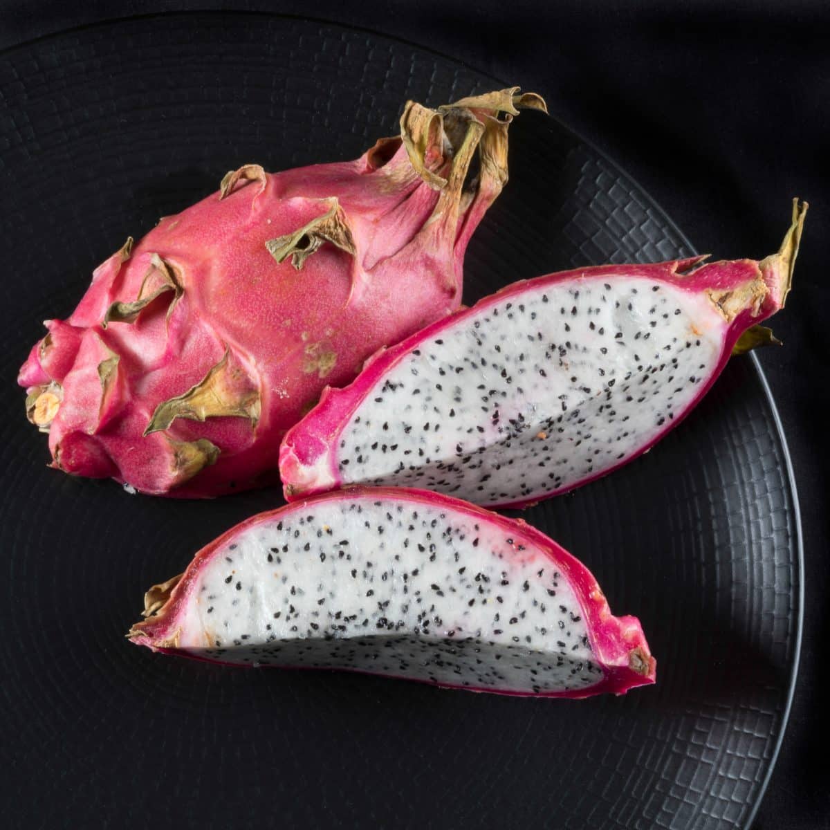 A sliced open dragon fruit showing white flesh with black seeds