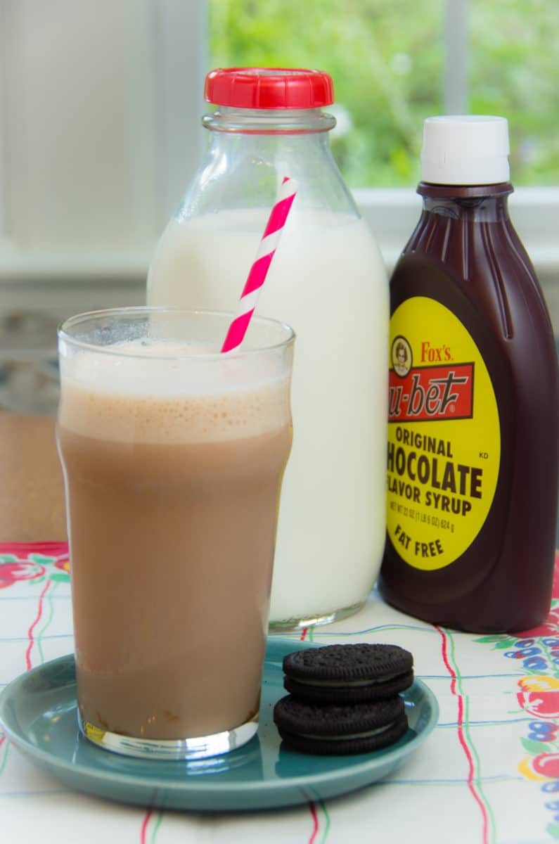 A glass of egg cream soda accompanied by two Oreo cookies.