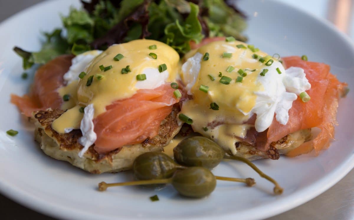 Poached eggs on smoked salmon with hollandaise sauce, capers, and greens on a plate