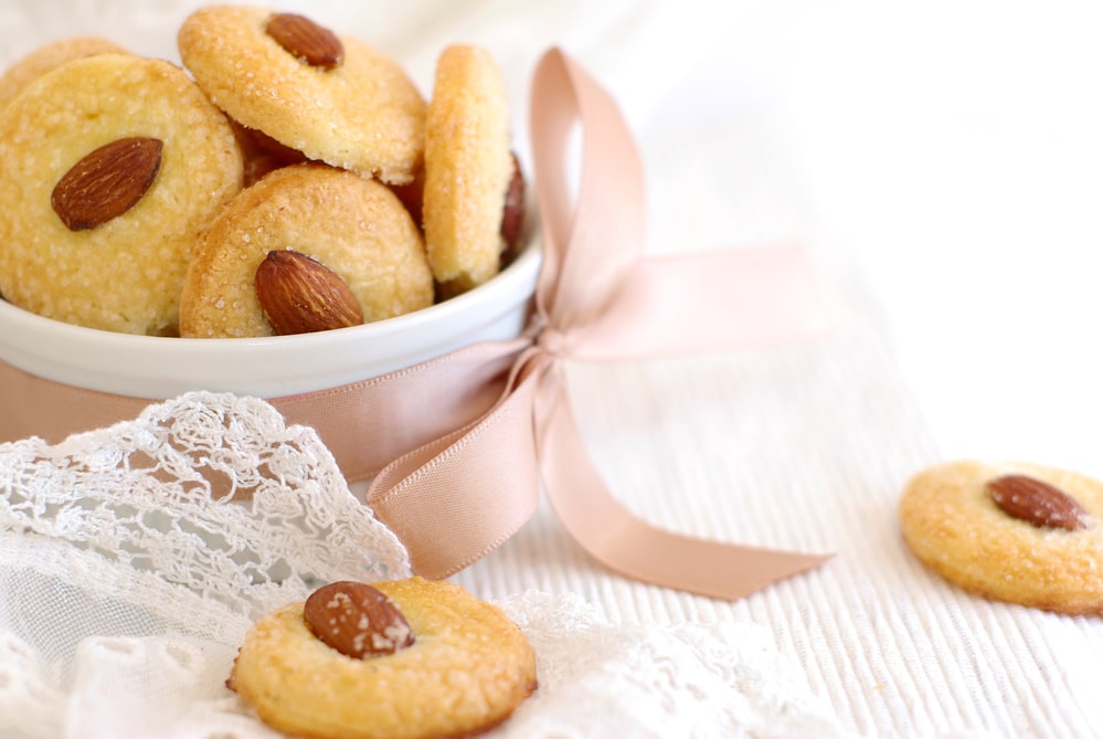 Delicate cookies topped with almonds, presented in a dish with a ribbon and lace