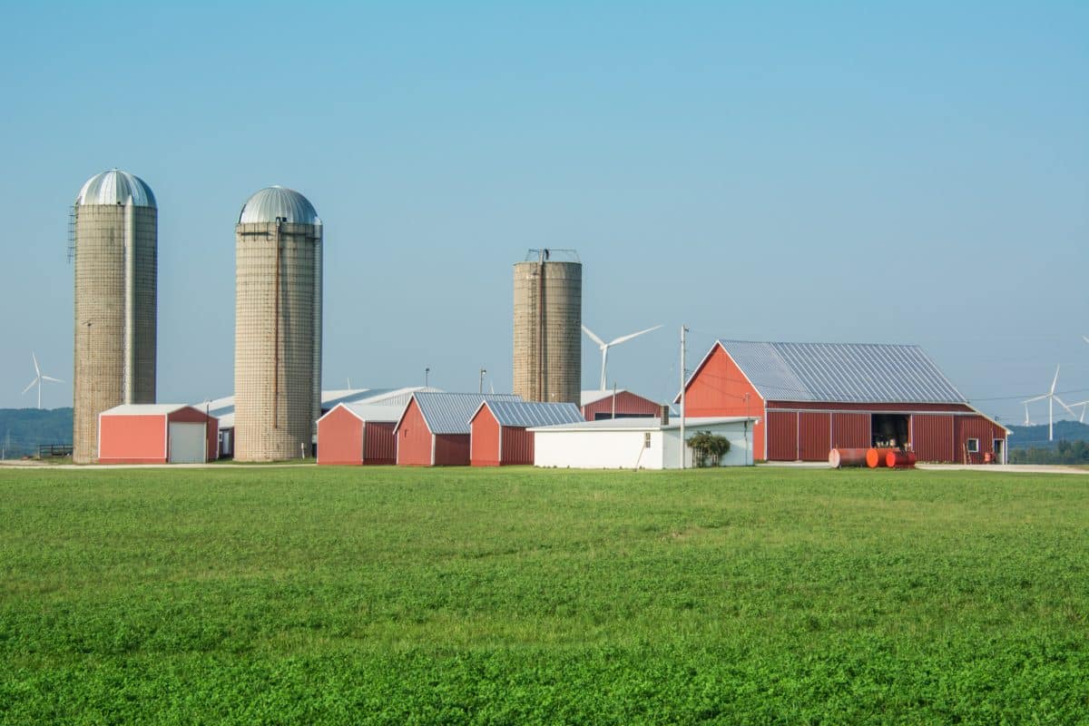 Panoramic view of farm silos and wind turbines in a green field.